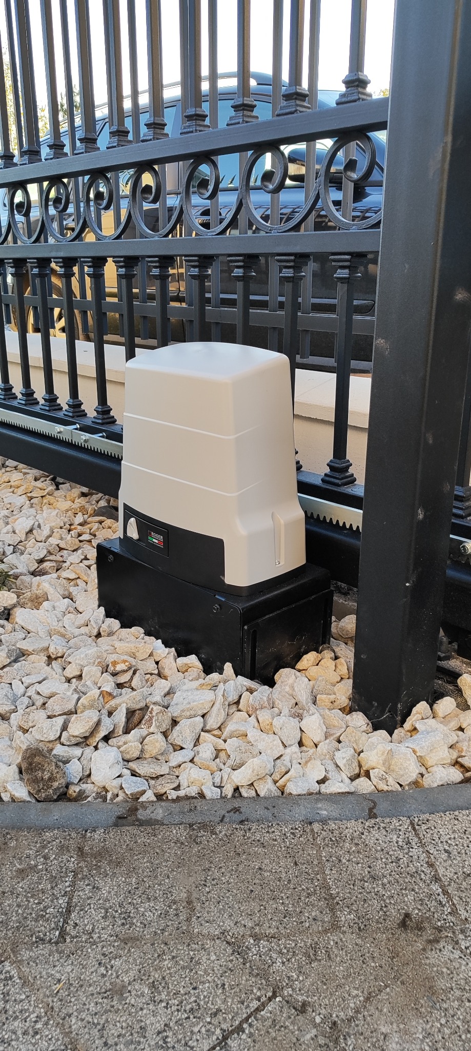 Zamontowany napęd do bramy przesuwnej marki Roger na tle ozdobnych kamieni i metalowego ogrodzenia. Widoczna listwa zębata.