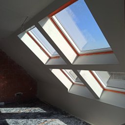 M.R TYNKI - Poddasze po nałożeniu gładzi gipsowej, widoczne okna dachowe i fragment ściany z cegły. Podłoga zabezpieczona folią malarską. Jasne wnętrze w trakcie wykańczania.