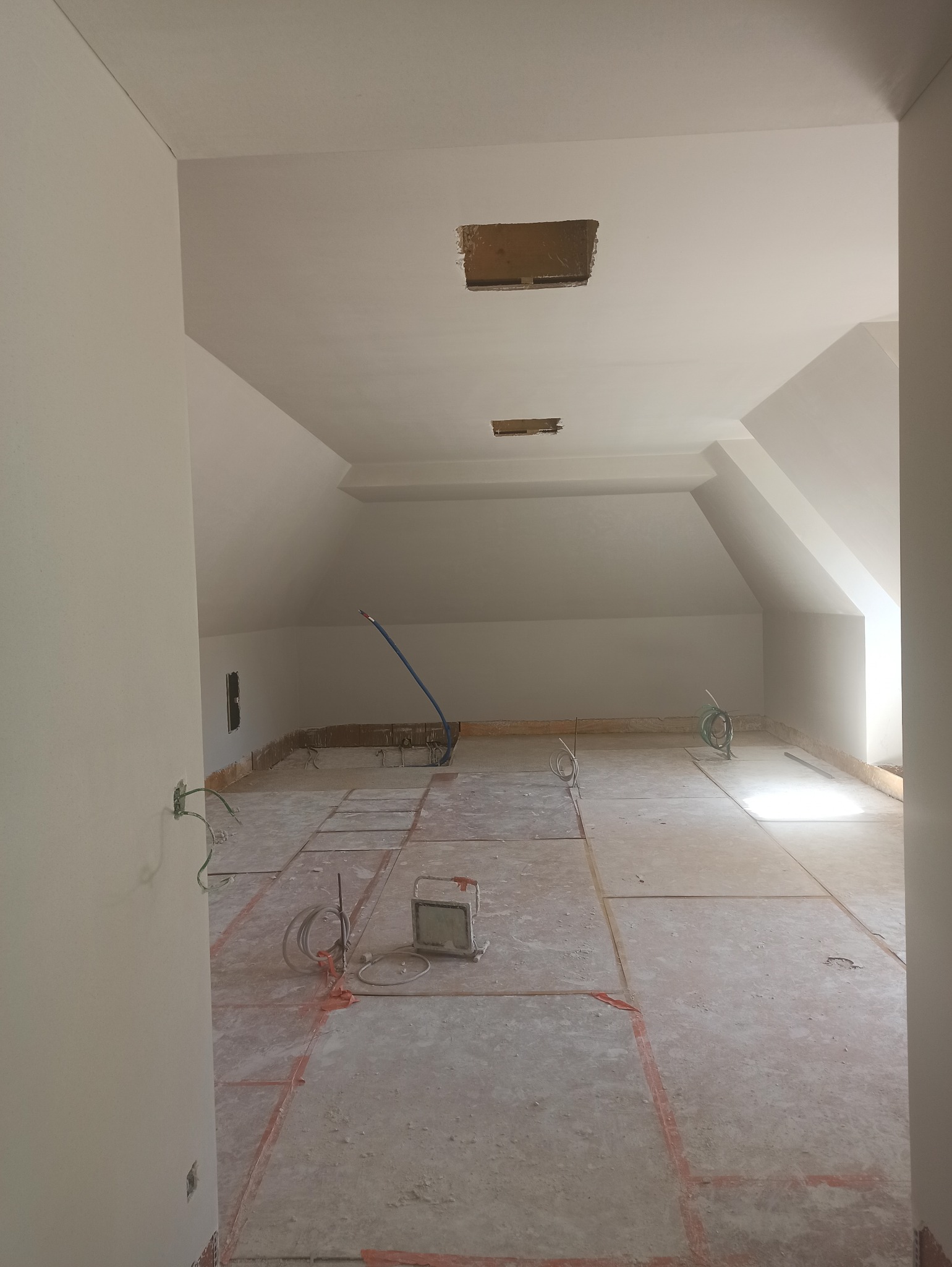 Poddasze w trakcie prac przygotowawczych do tynkowania: widoczne instalacje, kable, oraz zaznaczone obszary na podłodze. Otwory w suficie czekają na montaż.