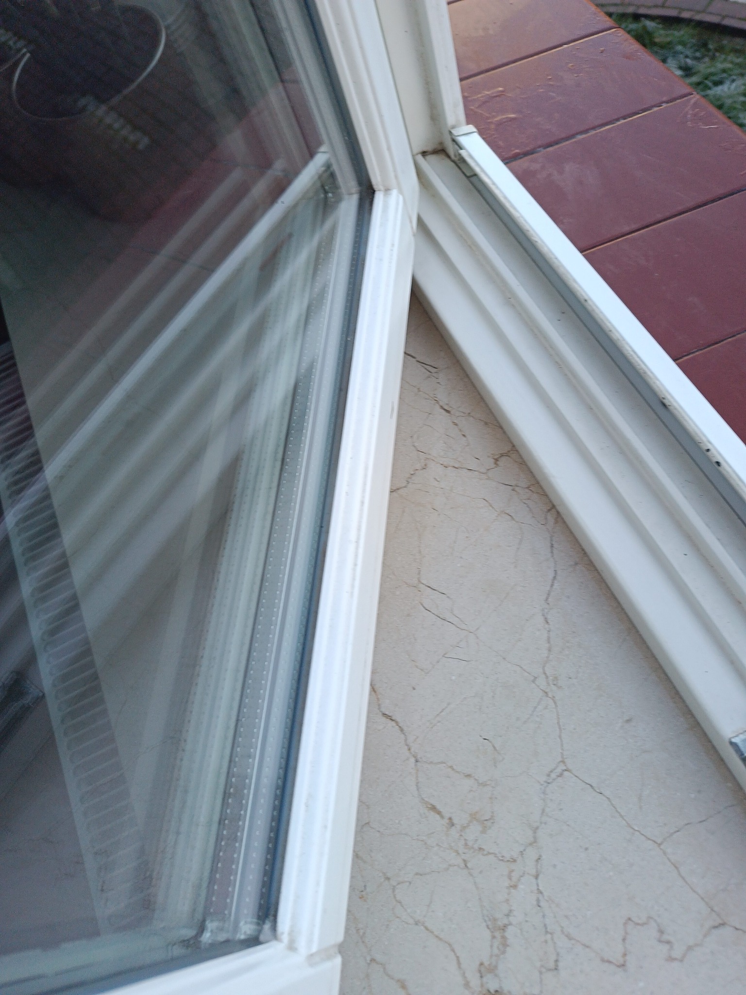 Otwarty, biały profil okienny z widocznym brudnym oknem i parapetem z marmurową fakturą. Na zewnątrz widoczne płytki i lekki szron.