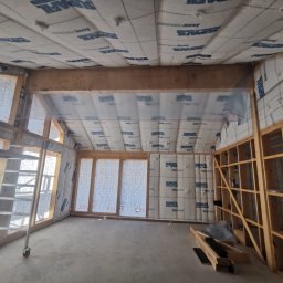 ENFORM Rafał Zulewski - Wnętrze domu w trakcie budowy, widoczne drewniane elementy konstrukcyjne, izolacja ścian i sufitu z folią Supafil, drabina oparta o ścianę, surowa podłoga.