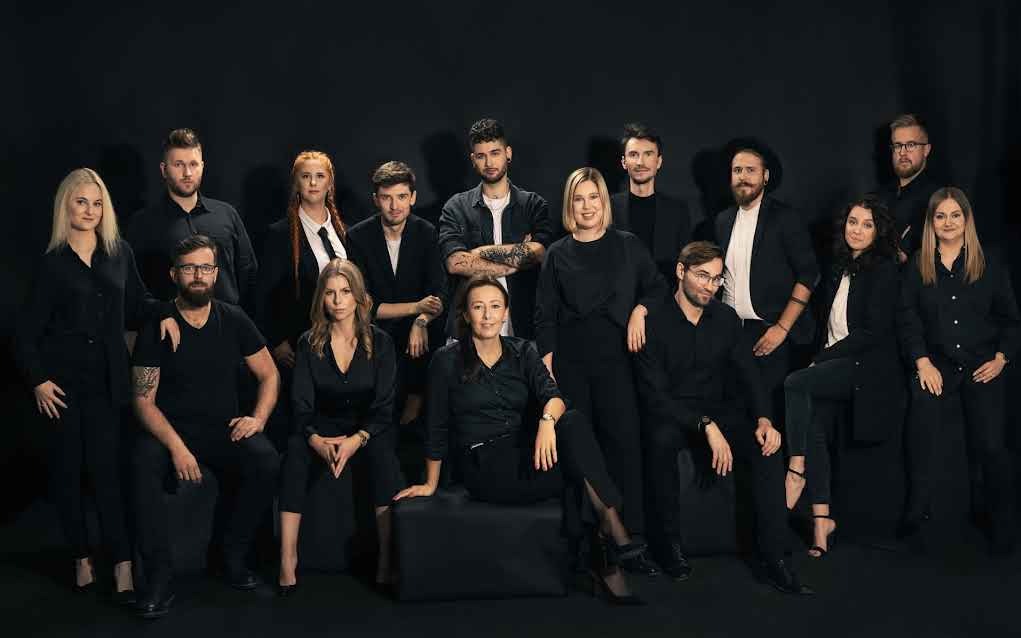 Zespół w czerni na ciemnym tle: portret grupowy pracowników agencji marketingowej, prezentujący profesjonalizm i zgrany team w branży reklamowej.