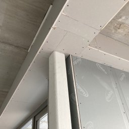 MAM Remonty - Montaż płyt gipsowo-kartonowych na suficie i ścianie, widoczne łączenia i wkręty. Elementy konstrukcyjne w trakcie prac wykończeniowych, surowy betonowy strop.