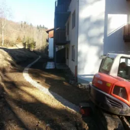 Wykonanie drenażu liniowego z użyciem minikoparki Kubota KX080-3a przy budynku mieszkalnym na zboczu wzgórza.