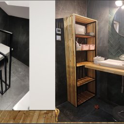 Adrian Lewandowski - Metalowy stojak na ręczniki i regał z drewnianymi półkami w łazience z szarą glazurą. Minimalistyczny design, czarne ramy, naturalne drewno.