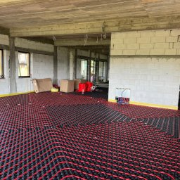 REM-BUD INSTAL BŁAŻEJ PĘDZIMĄŻ, ERYK PĘDZIMĄŻ SPÓŁKA CYWILNA - Czerwono-czarna instalacja ogrzewania podłogowego w surowym wnętrzu z białych bloczków, widoczne okna i kable. Żółta taśma wzdłuż ścian.