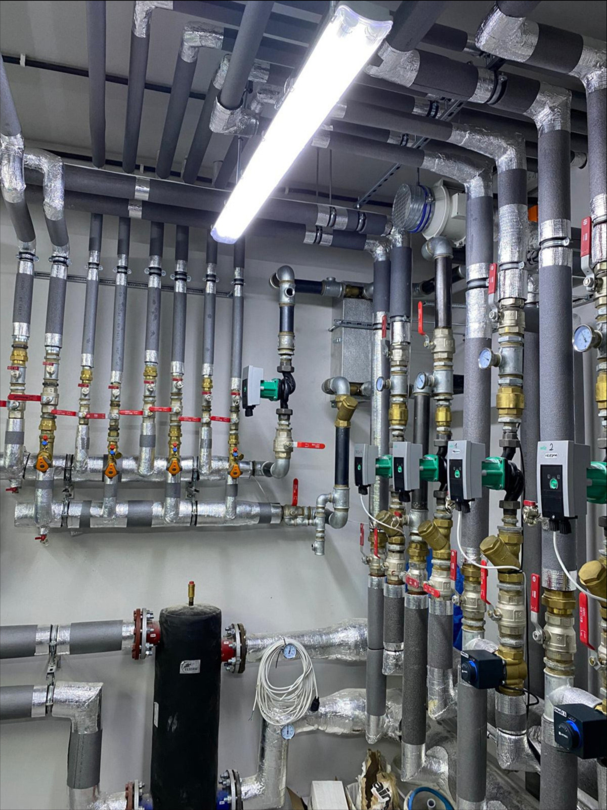 Złożona instalacja hydrauliczna z rurami izolowanymi termicznie, zaworami i czujnikami, oświetlona jarzeniówką, prezentująca profesjonalne wykonanie i dbałość o detale.