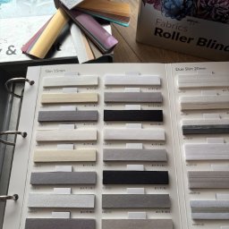 Patryk Kozak Rollkos - Katalog z próbkami tkanin do rolet wewnętrznych, prezentujący różne kolory i faktury materiałów. Widoczne oznaczenia kodowe próbek.