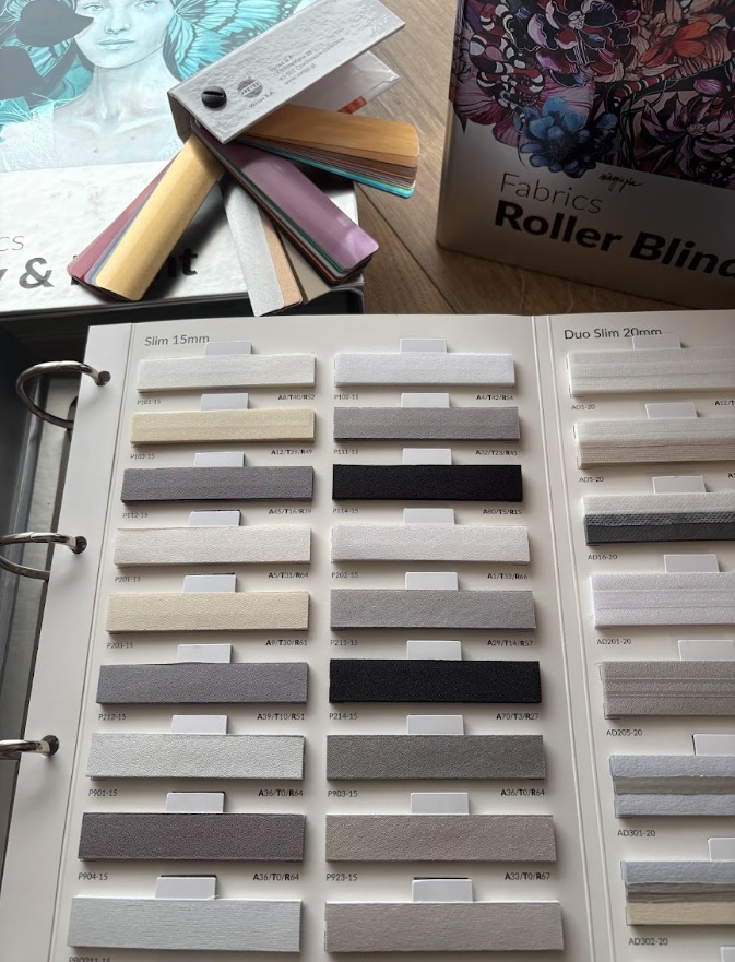 Katalog z próbkami tkanin do rolet wewnętrznych, prezentujący różne kolory i faktury materiałów. Widoczne oznaczenia kodowe próbek.