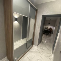 KOSTAGO Kostiantyn Kostenko - Szafa przesuwna z lustrami w przedpokoju, oświetlenie punktowe, marmurowe płytki podłogowe. Widok na jadalnię w głębi. Wykończenie wnętrz w szarościach i bieli.