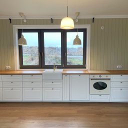 KOSTAGO Kostiantyn Kostenko - Jasna kuchnia w stylu rustykalnym: białe szafki z drewnianym blatem, okno z widokiem na zewnątrz, wiszące lampy. Ściany w odcieniach beżu. Podłoga drewniana.