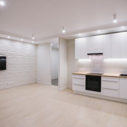 KOSTAGO Kostiantyn Kostenko - Nowoczesna, jasna kuchnia z białymi, błyszczącymi szafkami i drewnianym blatem. Na ścianie dekoracyjna, falista struktura i zawieszony telewizor. Minimalistyczne oświetlenie.