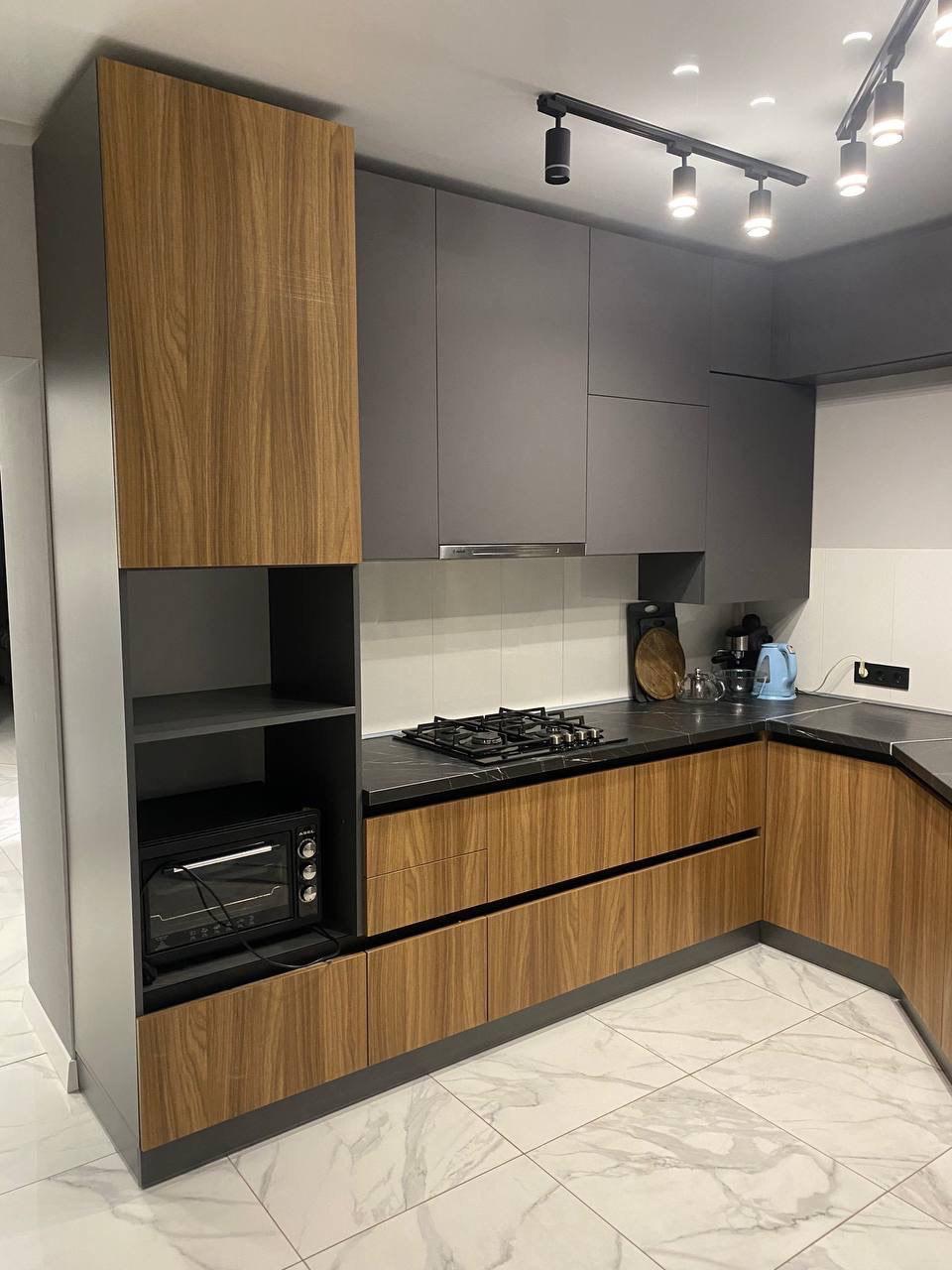 Nowoczesna kuchnia z szarymi szafkami i drewnianymi frontami, czarnym blatem i marmurową podłogą. Oświetlenie punktowe na suficie.