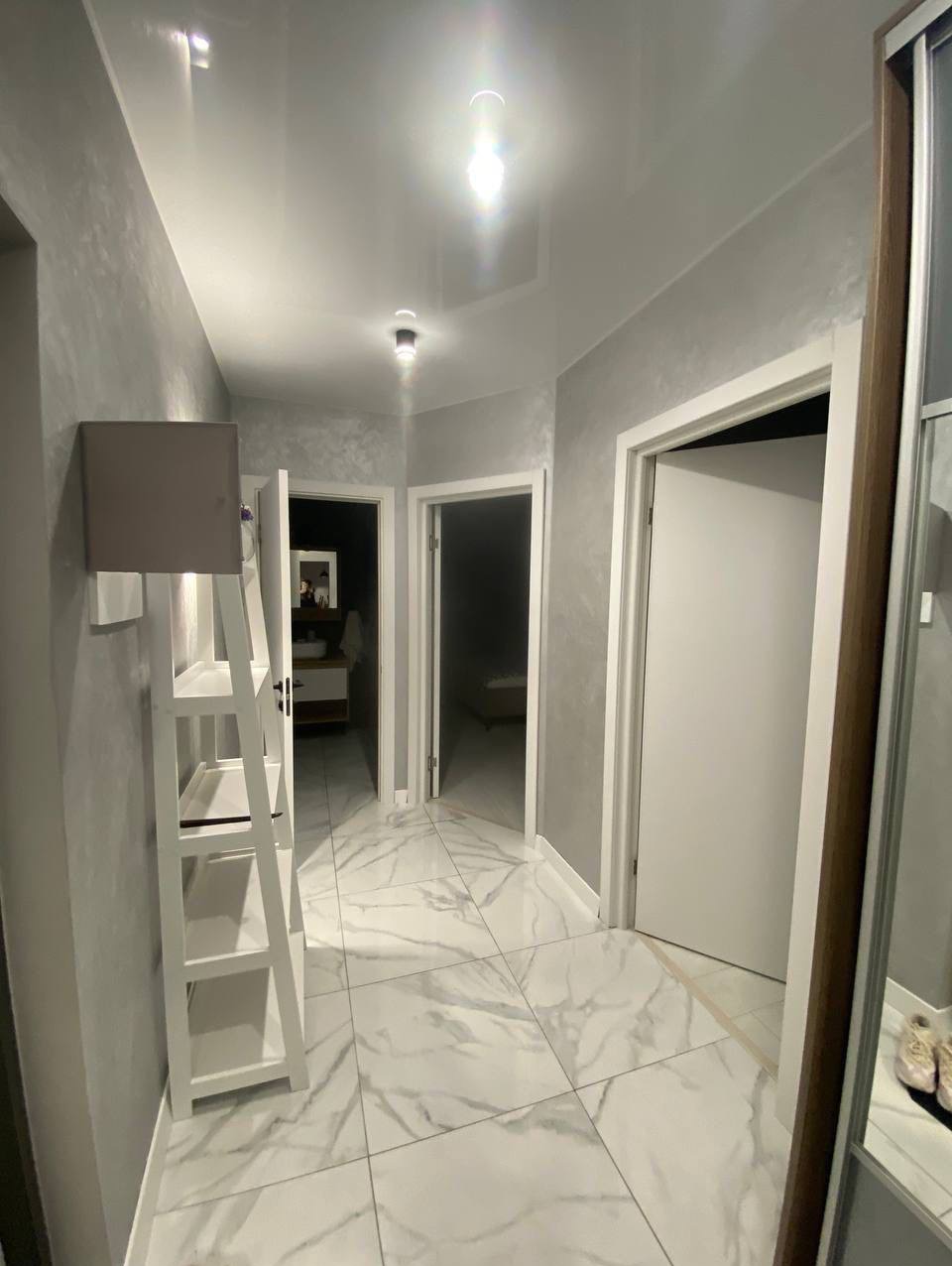 Korytarz po remoncie: białe marmurowe płytki podłogowe, szare ściany z efektem dekoracyjnym, białe drzwi i sufit napinany z oświetleniem punktowym.