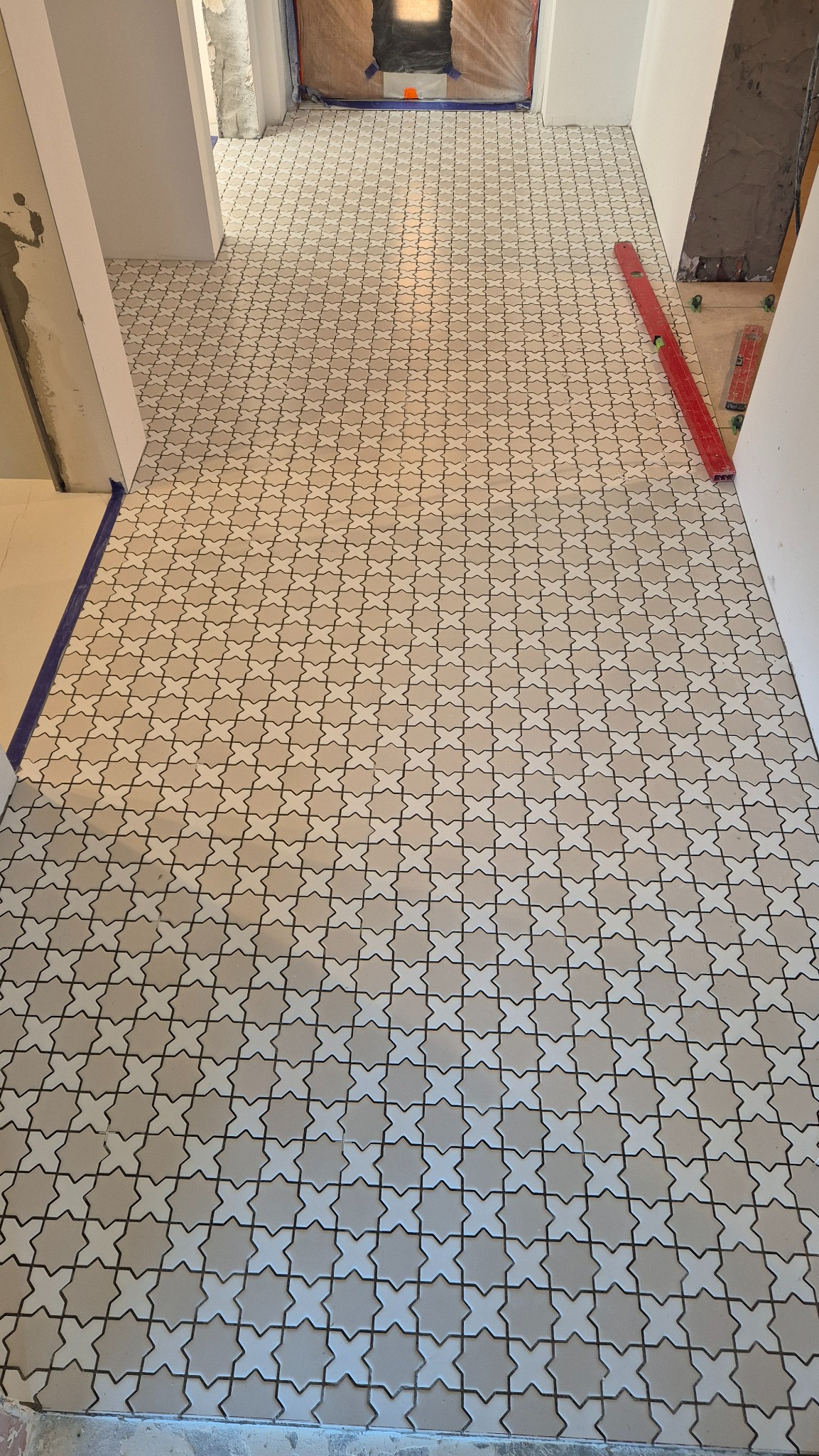 Ułożona, wzorzysta podłoga z płytek w odcieniach beżu i bieli, widok z perspektywy wejścia do pomieszczenia. Czerwona poziomica leży przy ścianie.