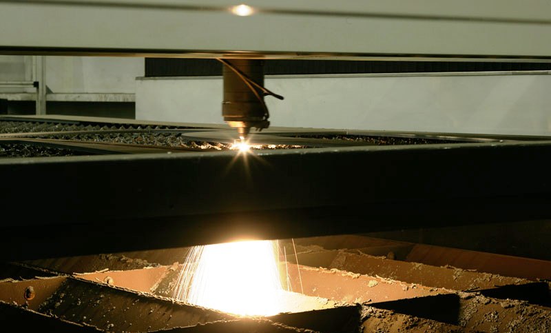 Proces cięcia metalu za pomocą lasera, widoczne iskry i urządzenie tnące