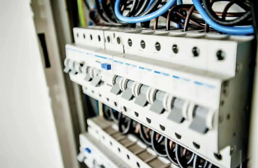 Rozdzielnia elektryczna z widocznymi bezpiecznikami i przewodami w kolorach niebieskim, czarnym i brązowym. Widok z boku, z bliska.