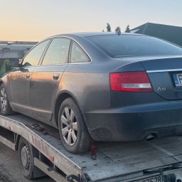Pomoc Drogowa A4 S19 Laweta Sokołów - Szary samochód osobowy marki Audi A6 na platformie pomocy drogowej, widok z tyłu, tablica rejestracyjna RZ 6882F, w tle dom i zachodzące słońce.