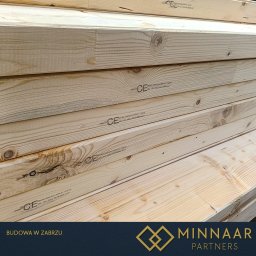 MINNAAR PARTNERS SPÓŁKA Z OGRANICZONĄ ODPOWIEDZIALNOŚCIĄ - Stos jasnych, heblowanych desek z widocznymi słojami i oznaczeniem CE, ułożonych równo jeden na drugim. Drewno przygotowane do budowy.