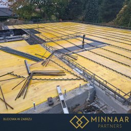 MINNAAR PARTNERS SPÓŁKA Z OGRANICZONĄ ODPOWIEDZIALNOŚCIĄ - Żółty szalunek stropowy z ułożonym zbrojeniem na fundamencie. Widoczne narzędzia budowlane i elementy konstrukcyjne. Budowa w Zabrzu.