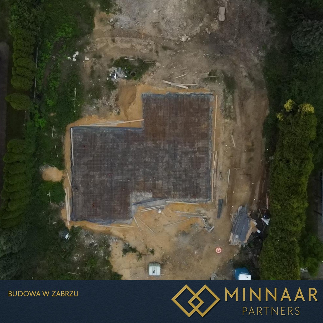 Widok z góry na zbrojenie fundamentów domu jednorodzinnego na działce budowlanej, otoczonej zielenią. Etap przygotowania do wylania betonu.