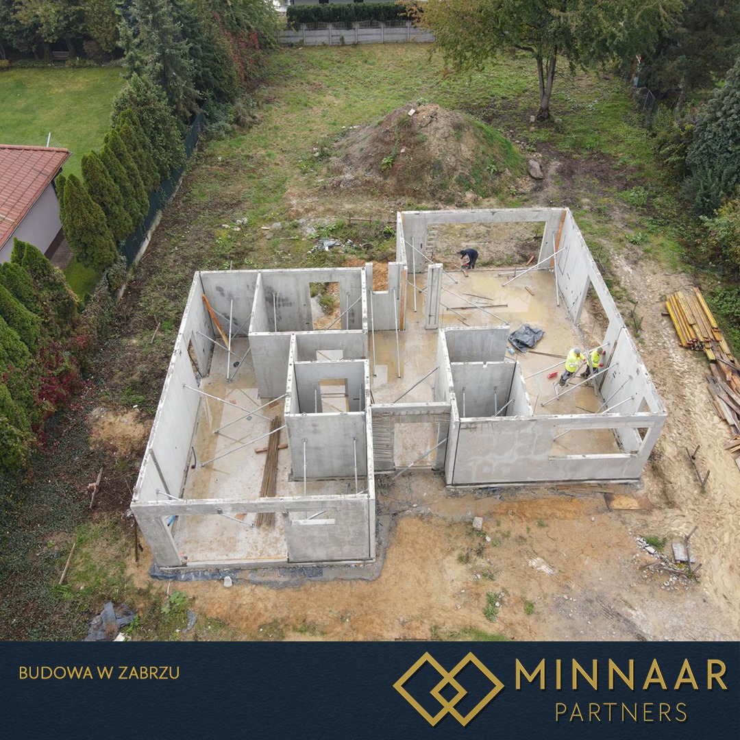 Budowa domu z prefabrykatów żelbetowych w Zabrzu, widok z góry. Widoczne ściany nośne i działowe, dwóch pracowników w żółtych kamizelkach i sterty drewna.