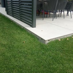 Yrek Horhus - Nowoczesny taras z jasnych płyt, obrzeża z kostki, ciemne lamele i meble ogrodowe. Soczysta zieleń trawnika. Minimalistyczny design.