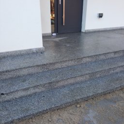 Yrek Horhus - Granitowe schody wejściowe z trzema stopniami prowadzące do nowoczesnego domu z szarymi drzwiami. Widoczne ślady piasku na kostce brukowej.