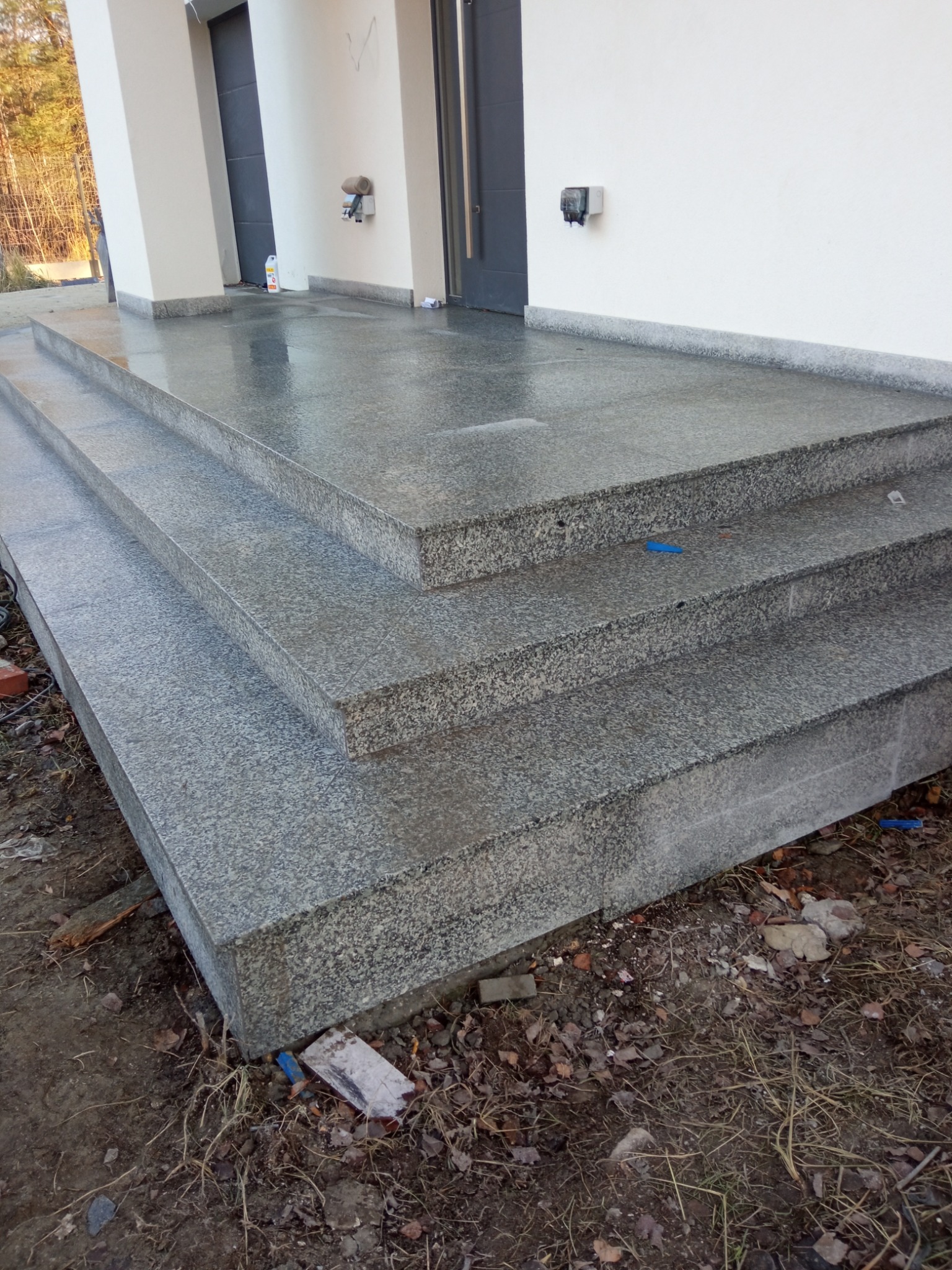 Granitowe schody zewnętrzne prowadzące do wejścia budynku, wykończone z dbałością o detale, z widoczną fakturą kamienia i elementami wykończeniowymi.