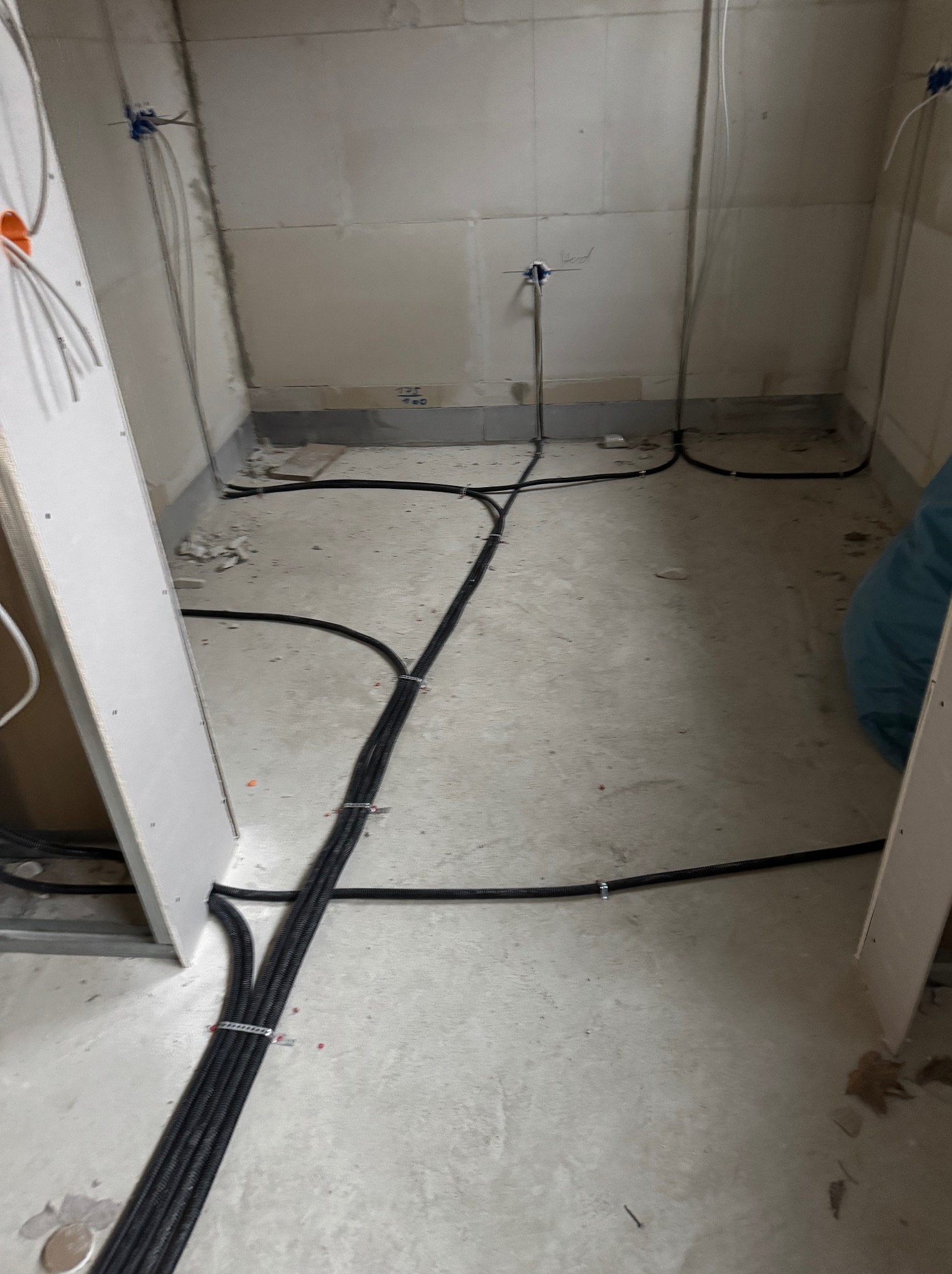 Wnętrze w trakcie prac: kable elektryczne w peszlach ułożone na podłodze, prowadzące do puszek instalacyjnych na ścianach. Widoczne płyty kartonowo-gipsowe.