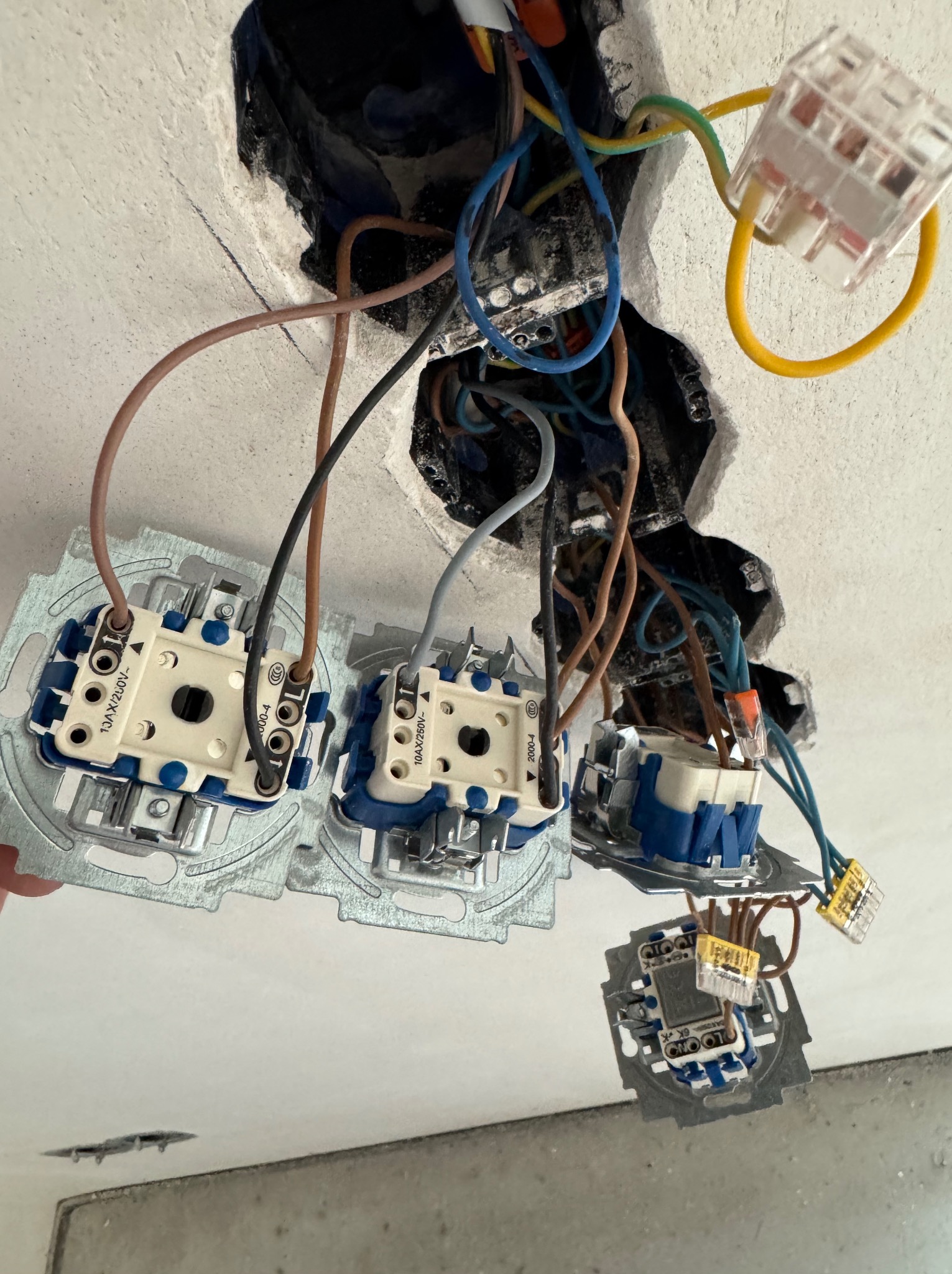 Fragment instalacji elektrycznej w suficie z widocznymi przewodami, kostkami WAGO i gniazdami w metalowych puszkach, w trakcie montażu. Widok z dołu.