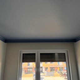 Bohdan Shulzhenko - Pomieszczenie po malowaniu: białe ściany, niebieski sufit z listwą, okno z roletami. Widok na budynek z zewnątrz. Nowoczesne wykończenie wnętrza.
