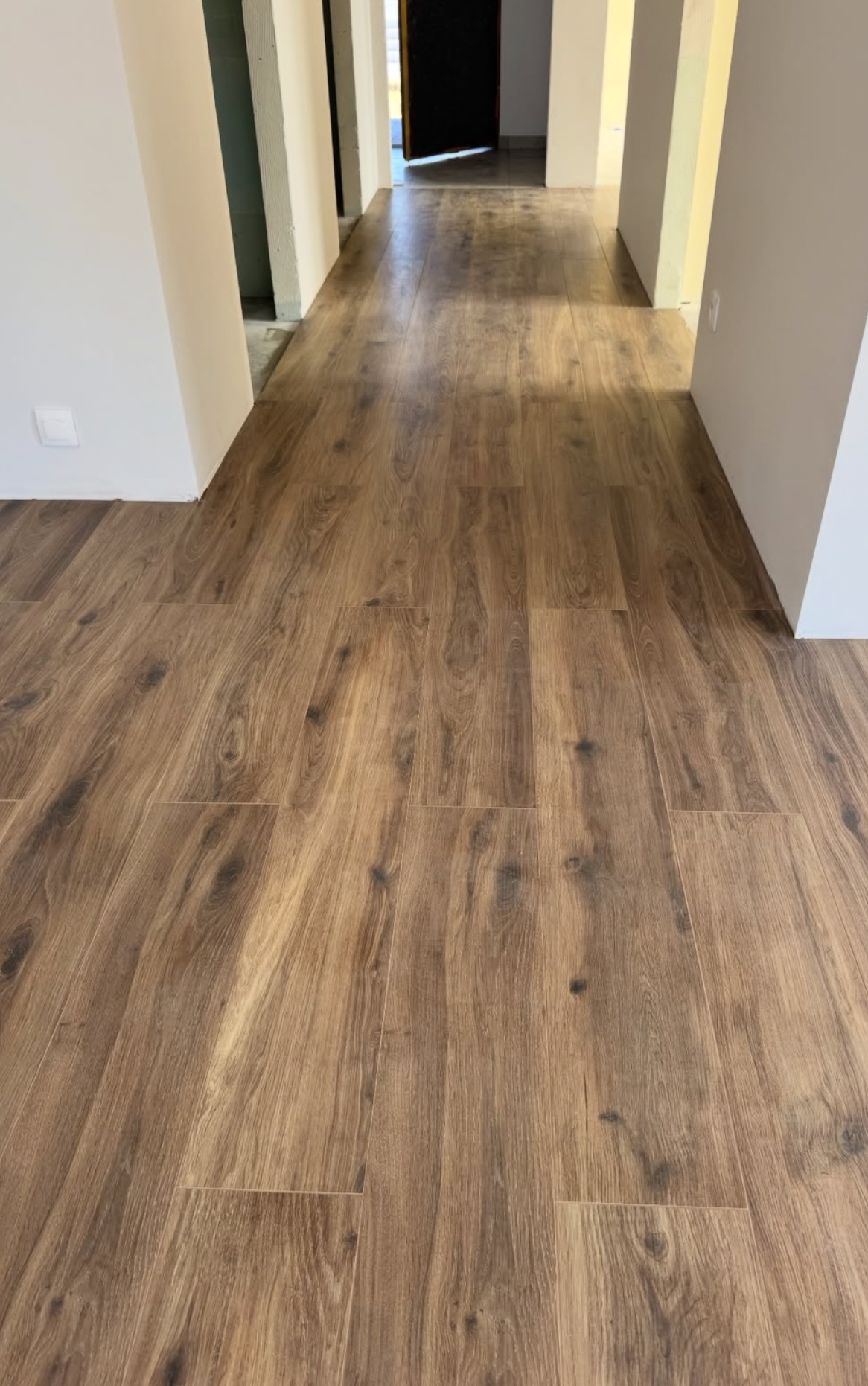 Ułożony parkiet w korytarzu, widok z perspektywy podłogi. Naturalne odcienie brązu desek, jasne ściany i widoczne przejścia do innych pomieszczeń.