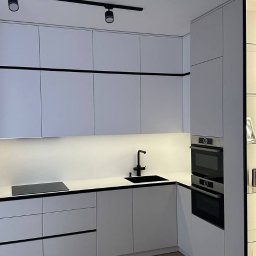 Profi Meble Oleksii Sainchyn - Nowoczesna kuchnia w bieli z czarnymi akcentami: minimalistyczne szafki, oświetlenie punktowe i drewniana podłoga. Ujęcie z perspektywy stołu z kwiatami.