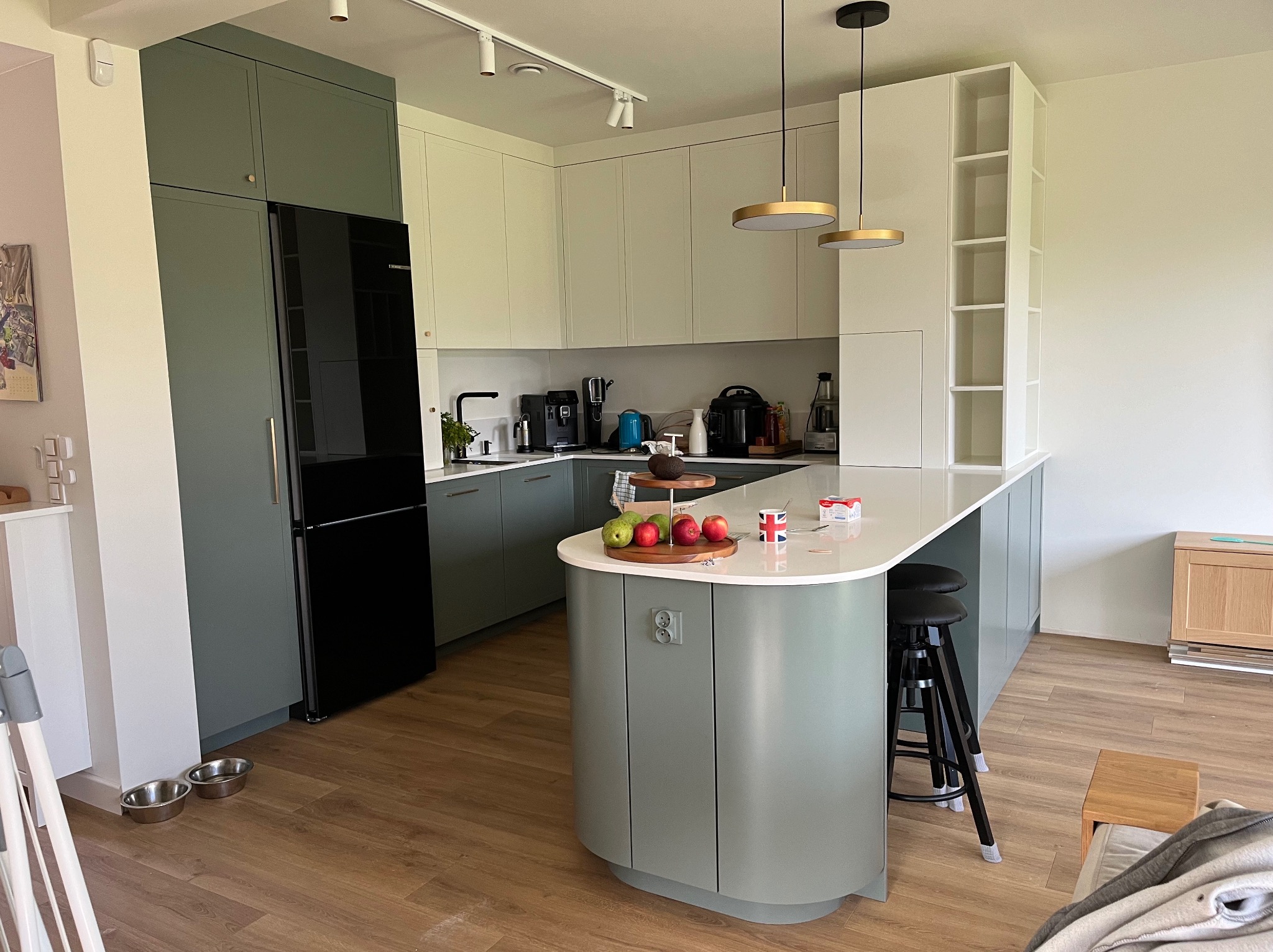 Nowoczesna kuchnia w odcieniach szarości i bieli z wyspą, oświetleniem punktowym i wiszącymi lampami. Widoczne sprzęty AGD i dekoracje.