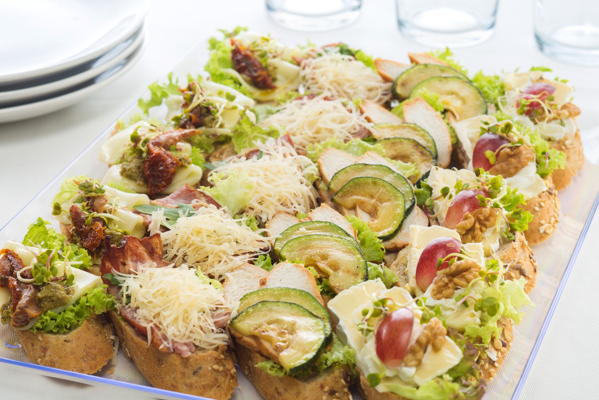 Dekoracyjne kanapeczki na tacy: różnorodne smaki, od suszonych pomidorów po grillowaną cukinię i brie z orzechami, idealne na elegancki catering.