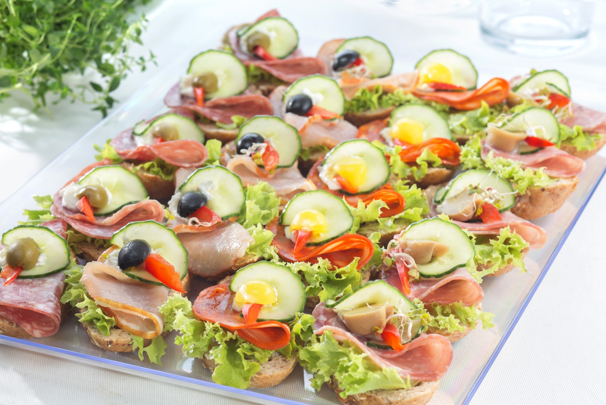 Eleganckie kanapeczki na tacy: różnorodne wędliny, świeży ogórek, sałata i kolorowe dodatki. Idealne na przyjęcie, z bliska widoczny tymianek.