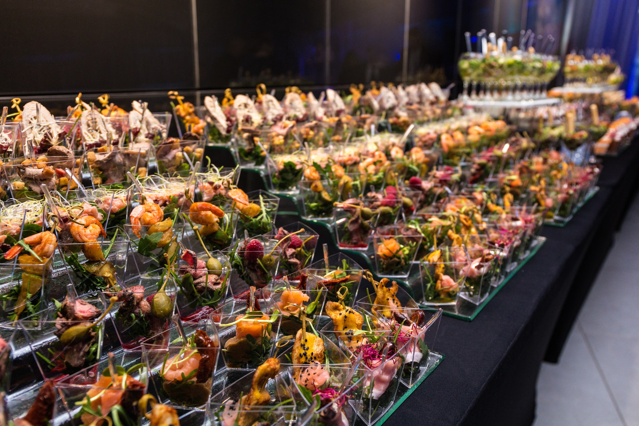 Bogato zastawiony stół z przekąskami w małych, przezroczystych naczyniach. Różnorodność smaków i kolorów, idealne na eleganckie przyjęcie. Widok z bliska, ostre detale.