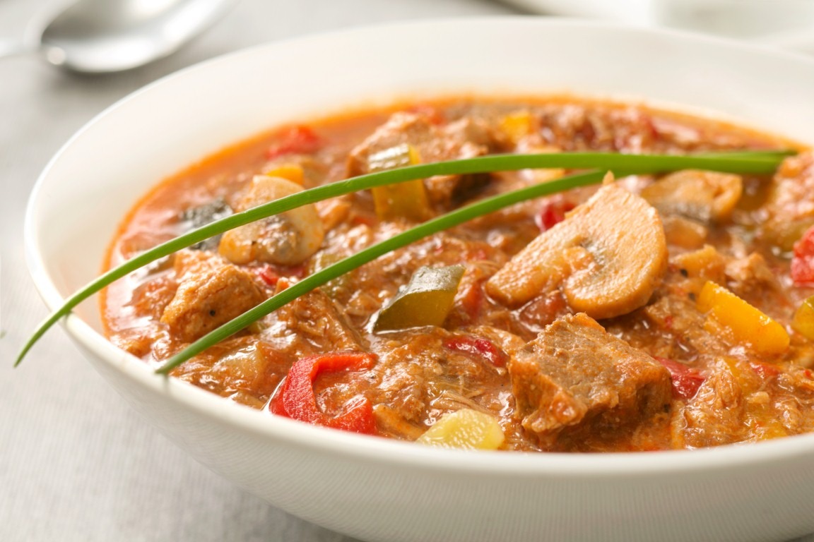 Aromatyczne danie gulaszowe z mięsem, papryką i pieczarkami, udekorowane świeżym szczypiorkiem, serwowane w białej misce. Idealne na catering.