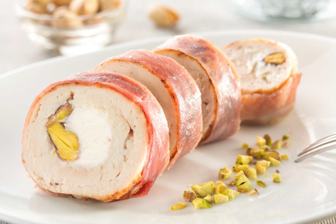 Rolada z kurczaka z pistacjami i szynką parmeńską na białym talerzu, zbliżenie. Elegancki catering świąteczny z Łodzi.
