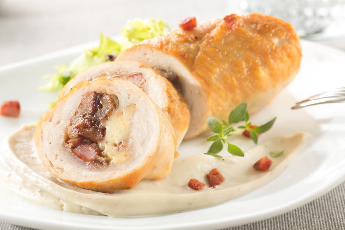 Rolada z kurczaka z farszem, pokrojona w plastry, podana na białym talerzu z sosem i dekoracją z ziół. Elegancka prezentacja dania.