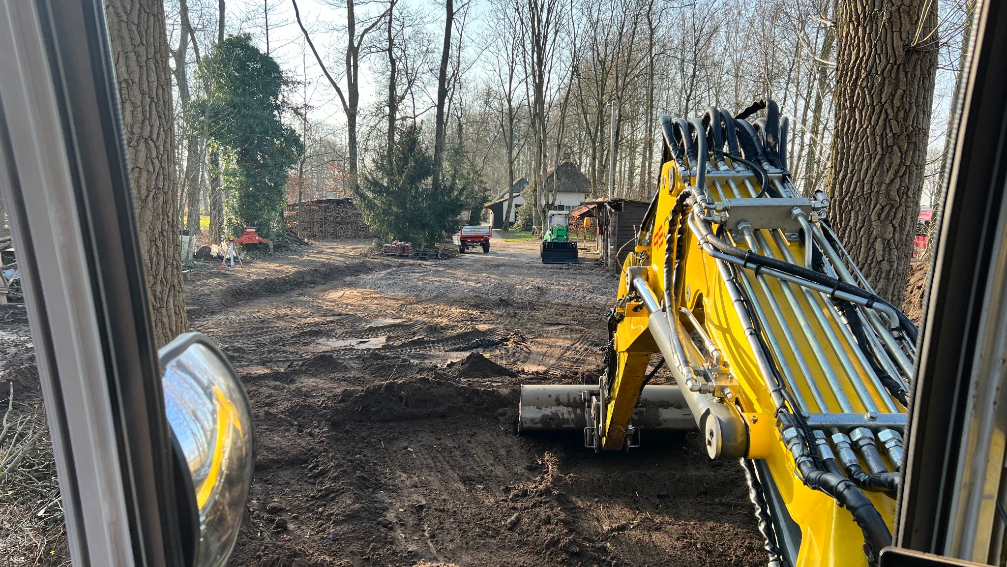 Żółta koparka w trakcie prac ziemnych w Józefowie, widok z kabiny. W tle drzewa i zabudowania, teren przygotowany pod dalsze prace.