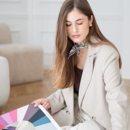 ALTITUDE ATTITUDE - Aleksandra Słojewska - Kobieta w beżowym garniturze siedzi na podłodze, trzymając paletę barw z napisem 'COOL SUMMER', w jasnym wnętrzu. Uwagę przyciąga apaszka i złote kolczyki.