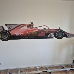 Mariusz Milej InkWall - Wielkoformatowy wydruk bolidu Formuły 1 Ferrari na ścianie, widoczny fragment toru jezdnego kamery. Realistyczne odwzorowanie detali, matowe wykończenie.