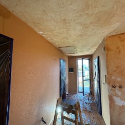 Wykończenia Premium WallPerfect - Pokój po malowaniu w Skomielnej Czarnej z zabezpieczonymi drzwiami folią. Widoczna drabina i wiadro. Ściany w odcieniach beżu i brązu, sufit z efektem dekoracyjnym.