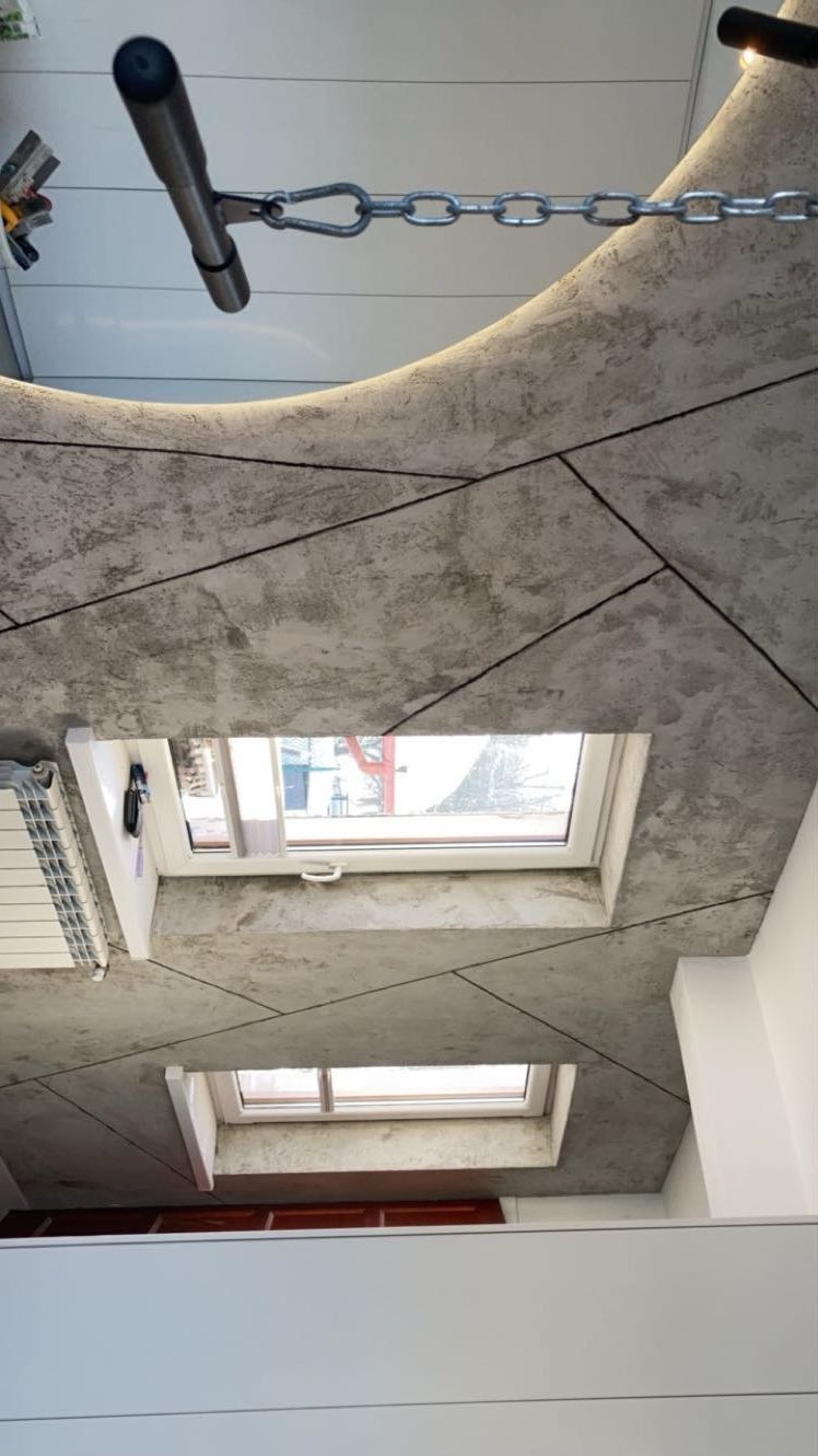 Betonowy sufit z dwoma oknami dachowymi i oświetleniem LED. Widoczny fragment grzejnika i szafki. Nietypowy kadr z dołu do góry.