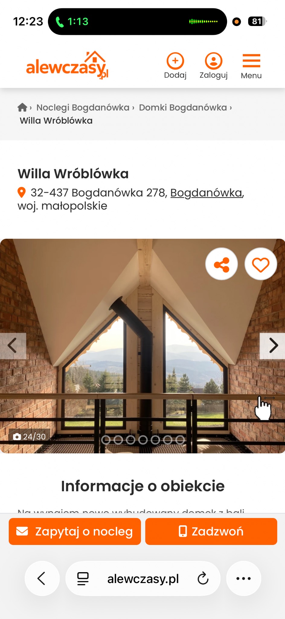 Wnętrze domku z bali z widokiem na góry. Ściany z cegły, drewniana konstrukcja dachu i komin. Widok z antresoli na krajobraz górski przez okna.