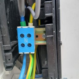 Józef Bujakowski - Niebieska kostka elektryczna z przewodami w skrzynce rozdzielczej, widoczne oznaczenia N, zbliżenie na połączenia kablowe w instalacji elektrycznej.