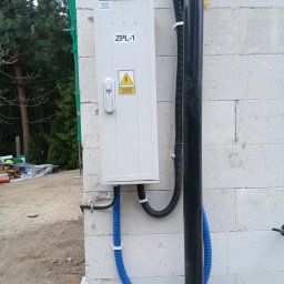 Józef Bujakowski - Zamontowana skrzynka elektryczna ZPL-1 na ścianie z betonu komórkowego, z widocznymi przewodami w peszlach. Na ścianie widoczna rura spustowa.