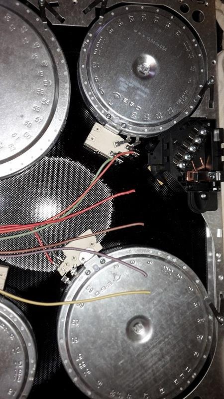 Wnętrze płyty indukcyjnej z widocznymi elementami grzejnymi, przewodami i modułem sterującym. Detal techniczny, ukazujący skomplikowaną budowę urządzenia.